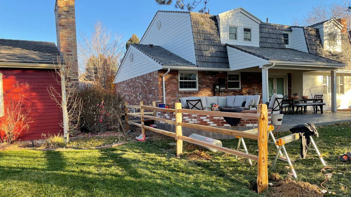 Split-rail fence going in — posts set, rails on, dirt still open at the post hole